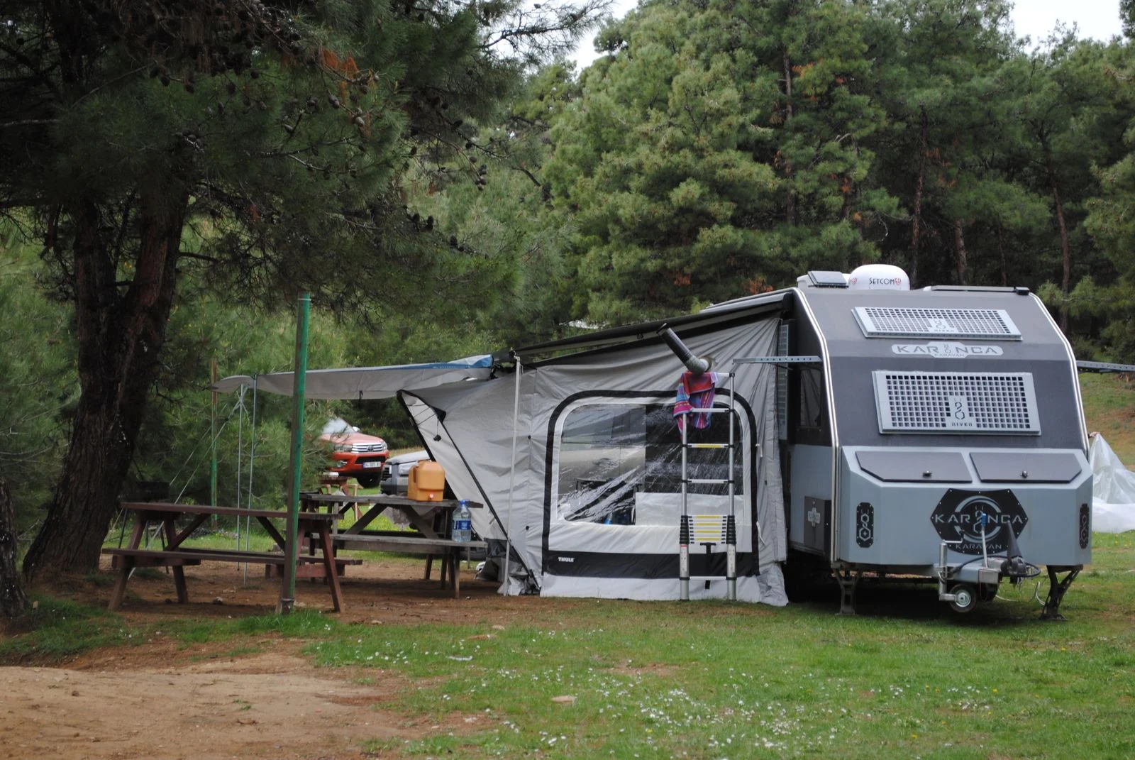 Caravane installée sur un emplacement de camping en forêt, avec des tables en bois