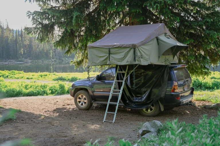Voiture équipée d’une tente de toit dans un camping en forêt, près d’un lac
